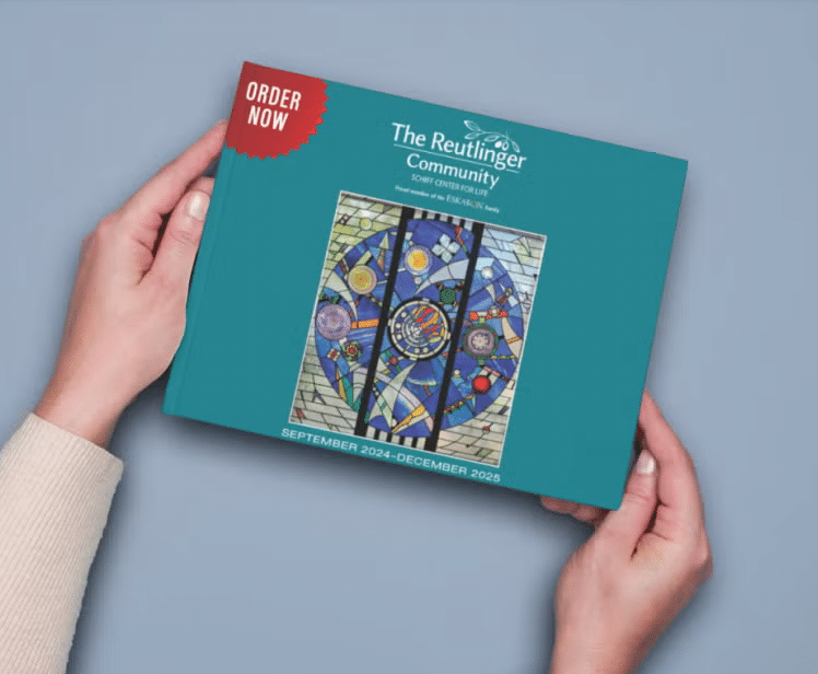 A person holds a teal book titled The Reutlinger Community with a colorful mosaic artwork on the cover and a red “Order Now” label. The bottom text reads “September 2024–December 2025.”.